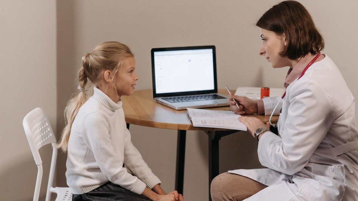 청원구 대상포진 예방접종 글 대표이미지 · 사진: Doctor in lab coat consulting a young girl in a clinic with a laptop on the table.